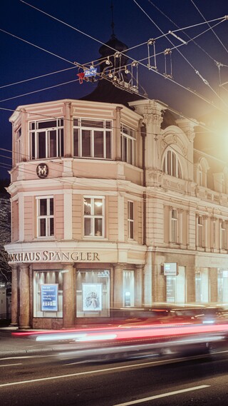 Ein schlossähnliches historisches Gebäude hinter den Umrissen von fahrenden Autos und Stromleitungen.