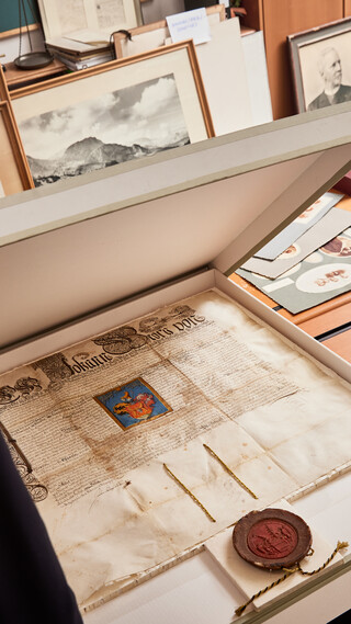 Mann in Anzug steht vor einem geöffneten Karton und betrachtet ein historisches Dokument.