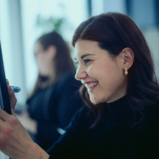 Eine Dame schreibt lachend auf einem Flipchart.