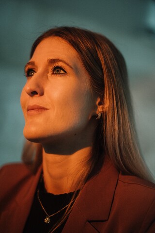 Dame mit blonden, langen Haaren im Portrait. Sie wird von vorne von einem warmen Licht angestrahlt.