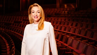 Eine lächelnde Dame steht zwischen den leeren Reihen eines Theaters.