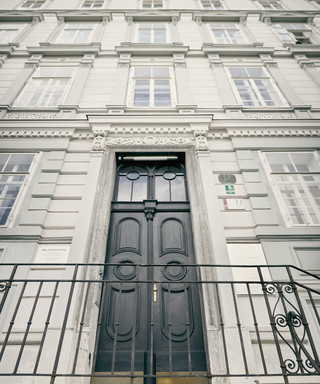 Fassade der Niederlassung Graz des Bankhaus Spängler. Graues Gebäude mit 4 Stockwerken, mehreren Fenster und einer schwarzen Tür. Ein Treppe mit Geländer dienen als Aufgang.