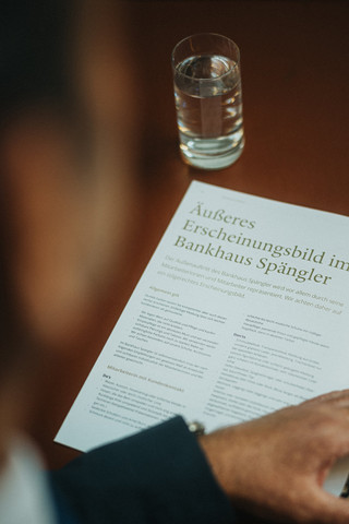Blick über die Schulter eines Herren, der ein beschriebenes Blatt liest.