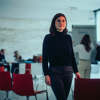 Eine Dame steht in einem modernen Raum mit geschäftigem Treiben.
