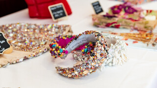 Designerstücke werden präsentiert. Ein Harrreifen mit Glitzersteinen ist ersichtlich.