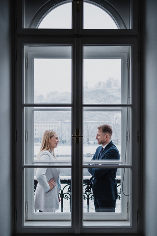 Hinter dem Fenster unterhalten sich eine Frau und ein Mann.