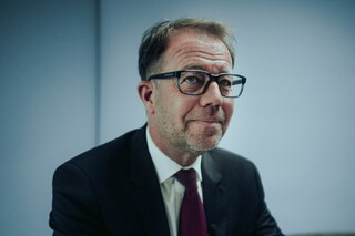 Ein Herr in Anzug sitzt lächelnd an einem Tisch.