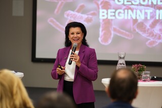 Prof. Anita Frauwallner, Gründnerin der Firma Omni Biotic, hält vor einem Publikum einen Vortrag in einem lila Sakko.