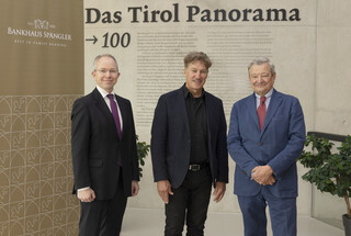 Drei Männer in Anzügen lächeln in die Kamera.