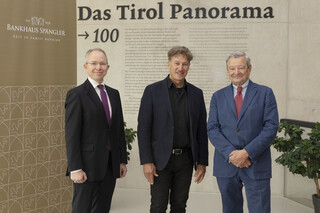 Drei Männer in Anzügen lächeln in die Kamera.