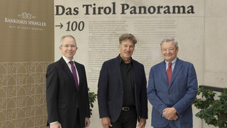 Drei Männer in Anzügen lächeln in die Kamera.