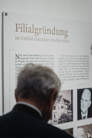Zwei Herren in Geschäftskleidung betrachten eine Informationstafel.