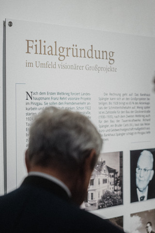 Zwei Herren in Geschäftskleidung betrachten eine Informationstafel.