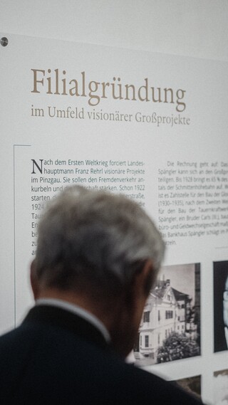 Zwei Herren in Geschäftskleidung betrachten eine Informationstafel.