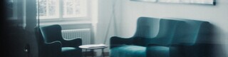 In einem Wohnraum befinden sich 2 kleine Tische, 2 Sessel und eine weiße Stehlampe.