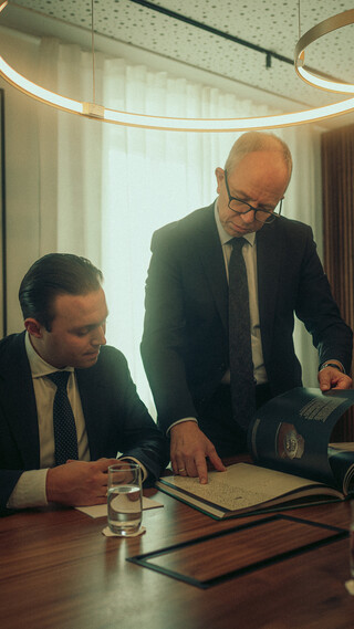 Beratungssituation: Ein Berater erklärt einem Ehepaar etwas und zeigt auf eine Broschüre.