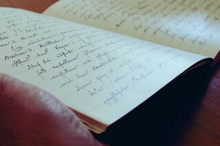 Hände halten ein aufgeschlagenes Notizbuch mit handschriftlichen Notizen.