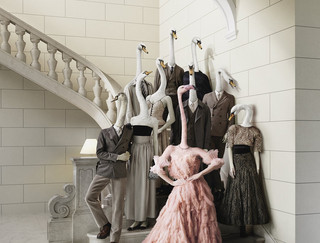 Webesujet des Bankhaus Spängler: Eine dunkel-gekleidete Familie mit Schwan-Köpfen steht auf einer Treppe. Eine Dame sticht besonders hervor - sie hat einen Flamingo-Kopf und trägt ein opulentes Kleid in rosa Farbe.