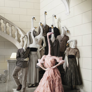 Webesujet des Bankhaus Spängler: Eine dunkel-gekleidete Familie mit Schwan-Köpfen steht auf einer Treppe. Eine Dame sticht besonders hervor - sie hat einen Flamingo-Kopf und trägt ein opulentes Kleid in rosa Farbe.