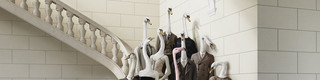 Webesujet des Bankhaus Spängler: Eine dunkel-gekleidete Familie mit Schwan-Köpfen steht auf einer Treppe. Eine Dame sticht besonders hervor - sie hat einen Flamingo-Kopf und trägt ein opulentes Kleid in rosa Farbe.