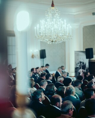 Publikum in Geschäftskleidung unter dem Kronleuchter eines historischen Saales.