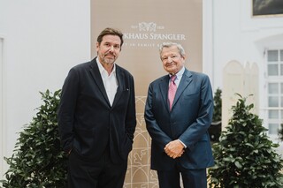 Zwei ältere Herren in Anzug posieren vor einem Rollup mit der Aufschrift "Bankhaus Spängler".