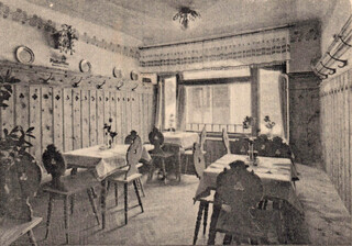 Ein historisches Schwarz-Weiß-Foto zeigt eine bäuerliche Gaststube mit Holzvertäfelung.