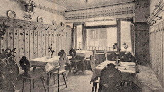 Ein historisches Schwarz-Weiß-Foto zeigt eine bäuerliche Gaststube mit Holzvertäfelung.