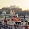 Stammhaus des Bankhaus Spängler in der Schwarzstraße 1 in 5020 Salzburg von oben. Barocke Kuppeln und eine dunkelrosa Fassade sind ersichtlich. Im Hintergrund sieht man die Festung Hohensalzburg und die Domkuppeln.