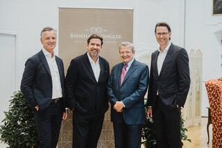 Vier Herren in Anzug posieren lächelnd vor einem Rollup mit der Aufschrift "Bankhaus Spängler".