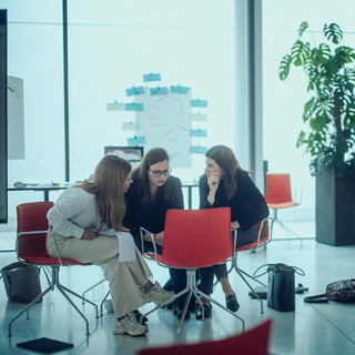 Drei Damen sitzen in einem modernen Saal in einer Reihe und kommunizieren miteinander.