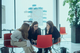 Drei Damen sitzen in einem modernen Saal in einer Reihe und kommunizieren miteinander.