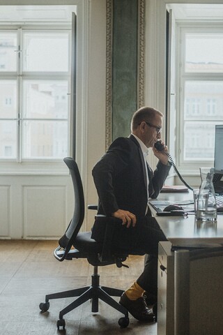 Ein Herr in Anzug telefoniert an einem Schreibtisch in einem historischen Büro.