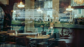 Blick durch eine Glasscheibe auf einen älteren Herrn in einem Kaffeehaus.