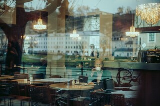 Blick durch eine Glasscheibe auf einen älteren Herrn in einem Kaffeehaus.