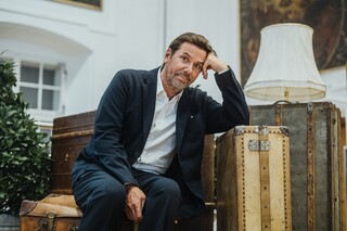 Ein Herr in Anzug posiert inmitten historischer Reisekoffer.