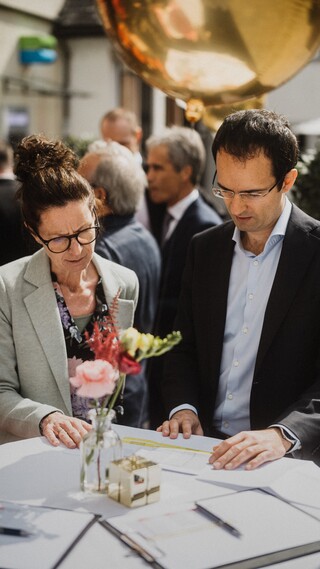 Eine Dame und ein Herr in Geschäftskleidung studieren konzentriert ein Dokument auf einem Stehtisch.