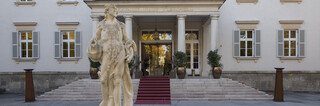 Historisches Gebäude "Kavalierhaus Klessheim" in Salzburg von außen. 3-stöckiges Gebäude mit Treppenaufgang und Statue vor Eingang.