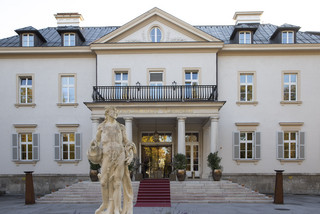Historisches Gebäude "Kavalierhaus Klessheim" in Salzburg von außen. 3-stöckiges Gebäude mit Treppenaufgang und Statue vor Eingang.