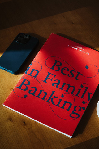 Eine Broschüre mit dem Titel "Best in Family Banking" liegt auf einem Tisch neben einem Smartphone.