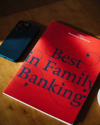 Eine Broschüre mit dem Titel "Best in Family Banking" liegt auf einem Tisch neben einem Smartphone.