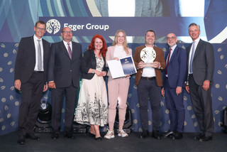 Eine Personengruppe in Geschäftskleidung posiert mit einer Trophäe vor einem Schild mit der Aufschrift "Egger Group".