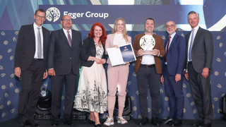Eine Personengruppe in Geschäftskleidung posiert mit einer Trophäe vor einem Schild mit der Aufschrift "Egger Group".