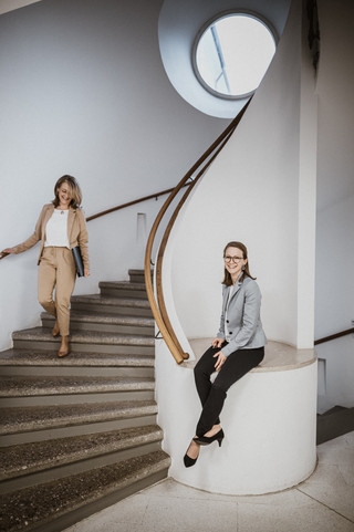 Eine Frau mit Brille und gelbem Kostüm geht eine Treppe hinunter.