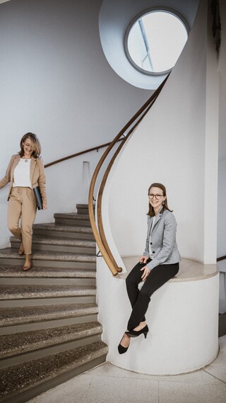 Eine Frau mit Brille und gelbem Kostüm geht eine Treppe hinunter.