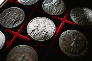 Schraubmünzen liegen in einer samtigen roten Box. Der Blick von oben zeigt die schön gestalteten, detailreichen Oberflächen der Münzen.