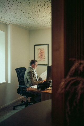 Ein Mann sitzt an seinem Schreibtisch und liest aufmerksam etwas. 