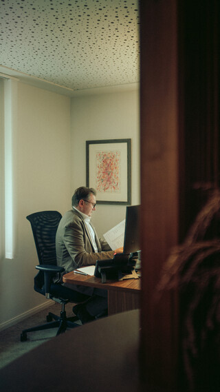 Ein Mann sitzt an seinem Schreibtisch und liest aufmerksam etwas. 