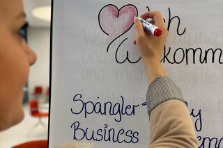 Eine Dame beschreibt ein Flipchartpapier mit dem Text "❤lich Willkommen".