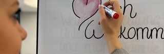 Eine Dame beschreibt ein Flipchartpapier mit dem Text "❤lich Willkommen".